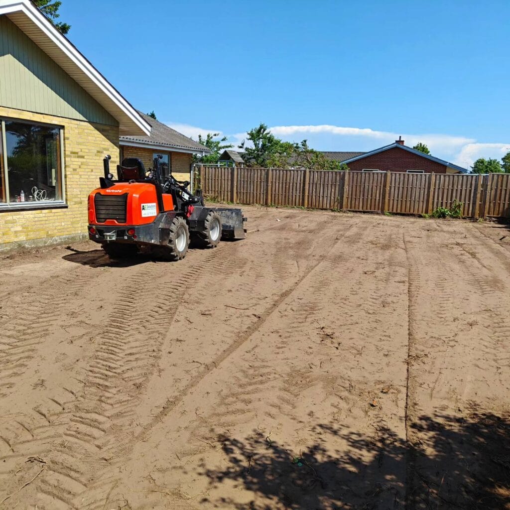 Rød minilæsser planerer jord i husets baghave